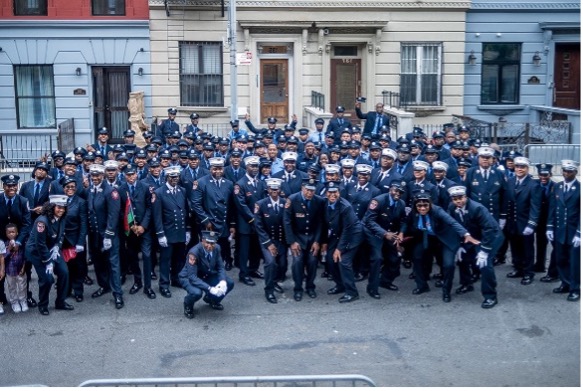 Rows of uniformed police officers pose in front of three building entranceways (from left to right, light blue, cream, light blue)