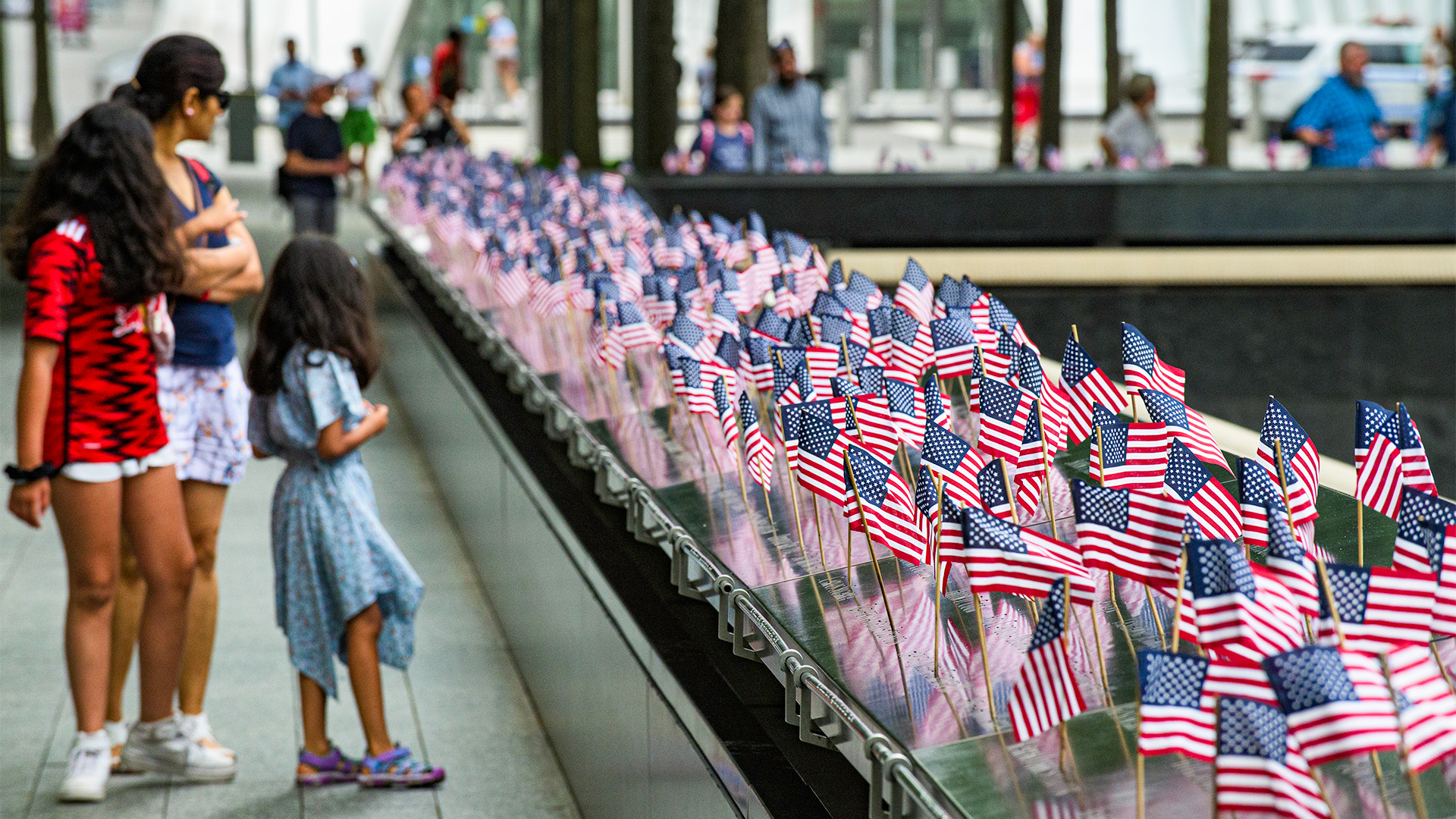 A small group including a toddler looks on at the Memorial, which is lined with small American flags at each victim's name