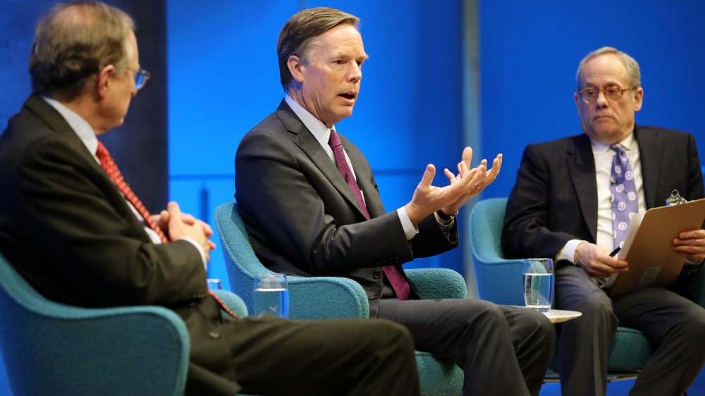 Former U.S. Ambassador to NATO R. Nicholas Burns gestures with both hands as he speaks onstage between former Deputy Secretary General of NATO Alexander Vershbow and Clifford Chanin, the executive vice president and deputy director for museum programs. Vershbow has his hands folded as he listens on. Chanin is holding a clipboard.