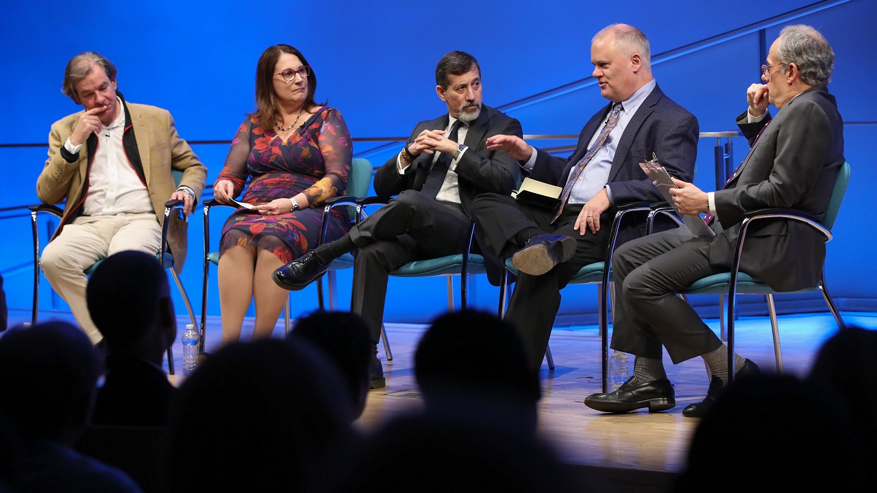 Mark Stout, who advised the Museum in the creation of the exhibition, speaks onstage at the Museum Auditorium as three people—al-Qaeda experts Peter Bergen, Bruce Hoffman and Mary E. Galligan—sit to his right looking on. Clifford Chanin, the executive vice president and deputy director for museum programs, sits to the left of Stout holding a clipboard. Audience members are silhouetted in the foreground.