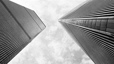 Low-angle view of the Twin Towers roaming into the cloudy sky. The height is emphasized by the towers' chamfered corners and closely spaced exterior columns.