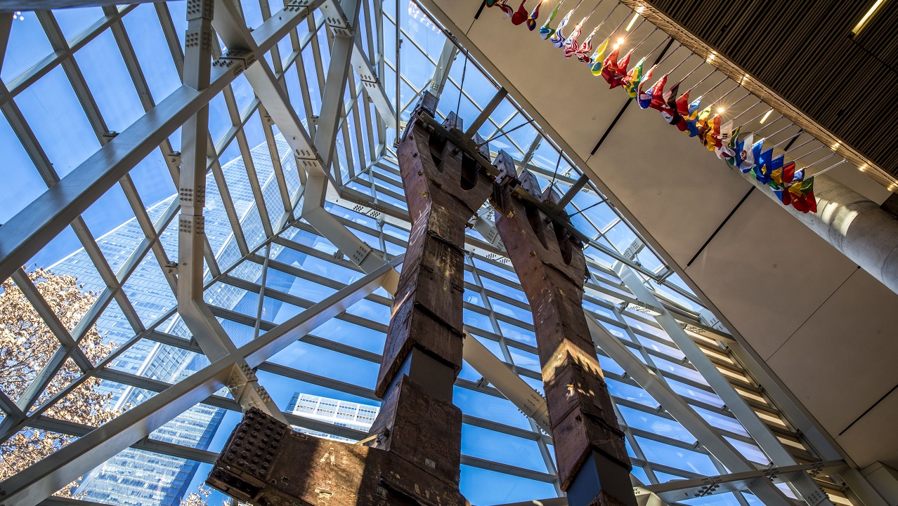 Two eighty-foot tall steel columns, known as the Tridents, tower over the interior of the museum Pavilion. One World Trade Center points skyward outside the windows.