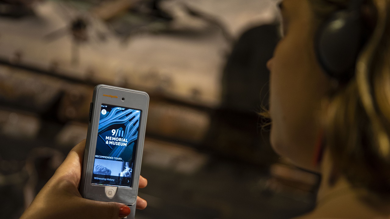 A woman holds up a listening device playing the 9/11 Memorial & Museum Audio Guide.