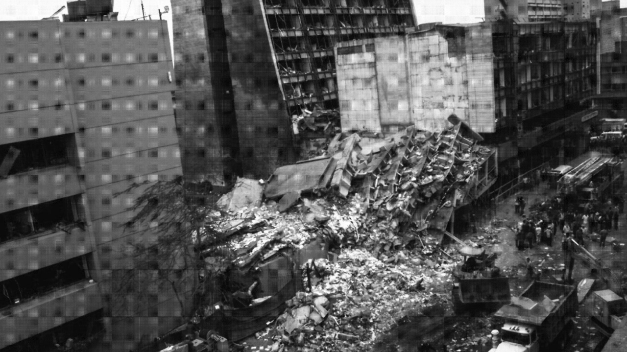 An aerial view of a destroyed building between partially damaged buildings.