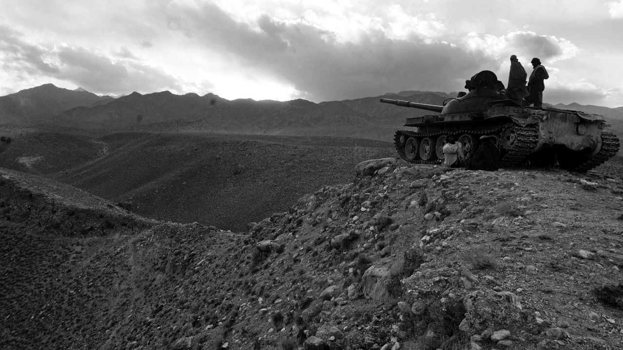 Two individuals standing on a tank overlooking a rocky desert landscape.”Two individuals standing on a tank overlooking a rocky desert landscape.