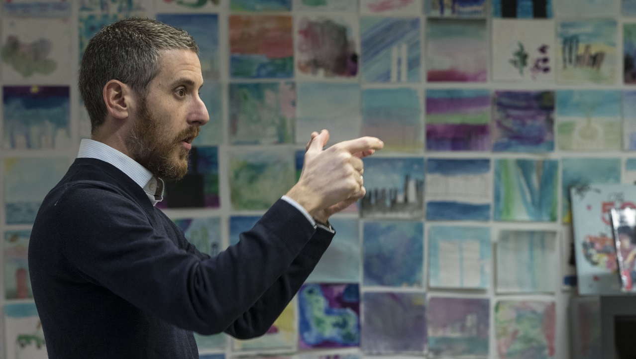 An educator speaks with his hands to an unseen audience of school children inside the Museum's classroom space.