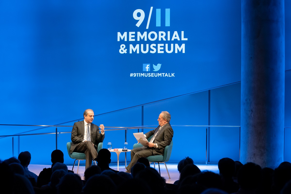 In this wide-angle view from the audience, Preet Bharara, the former U.S. attorney for the Southern District of New York, and moderator Clifford Chanin sit onstage at the Museum Auditorium during a public program. The silhouettes of audience members are in the foreground. Onstage Bharara is gesturing with his left hand as he speaks to Chanin, who is holding a clipboard.