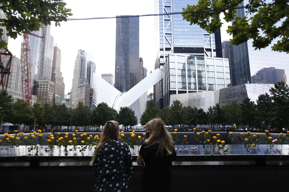 Two family members stand in front of dozens of yellow roses placed in the names parapet.