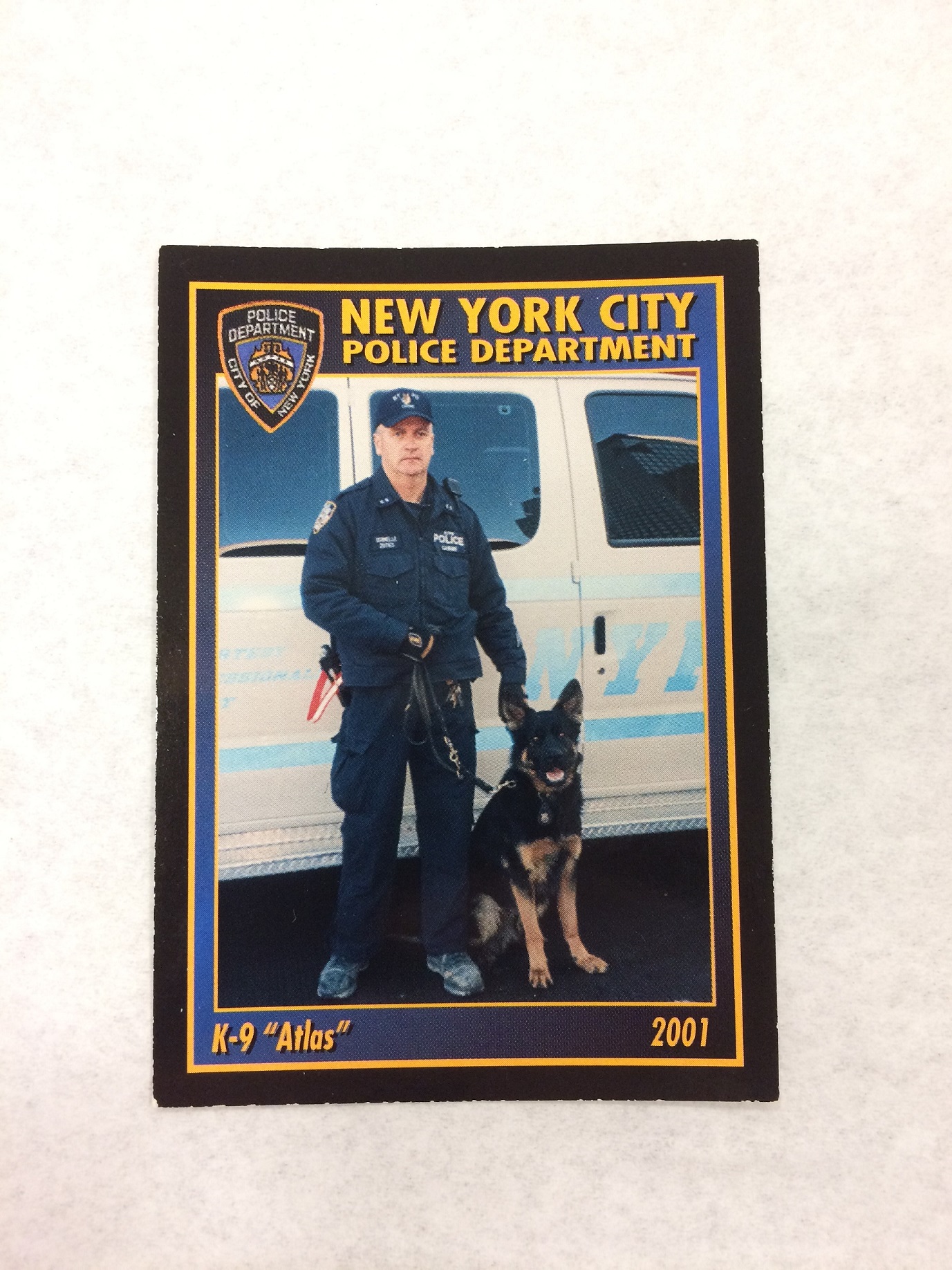 A postcard shows a police officer in uniform with his German Shepherd, standing in front of a white vehicle