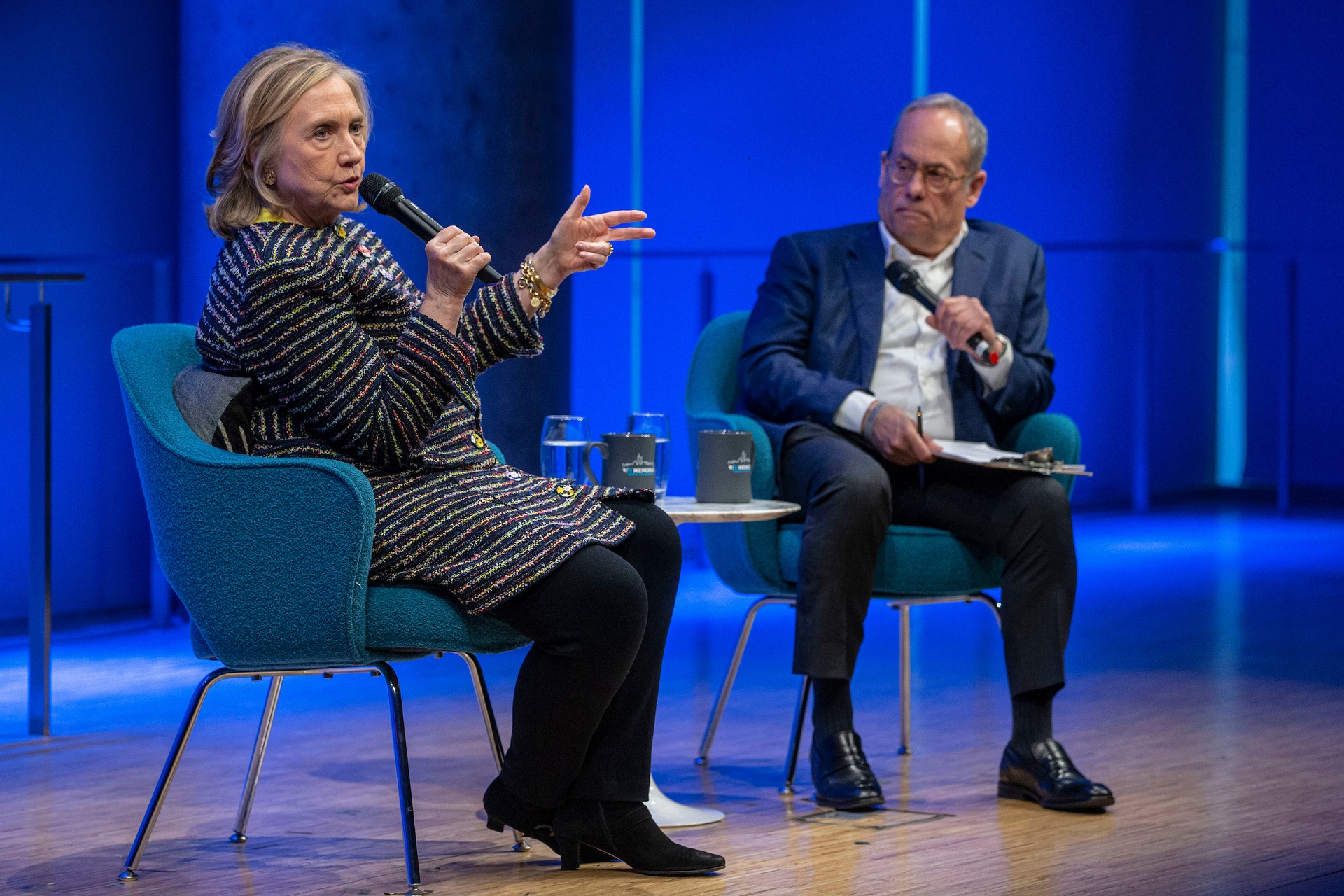 Hillary Rodham Clinton speaks, to the left of a man in a dark suit. 