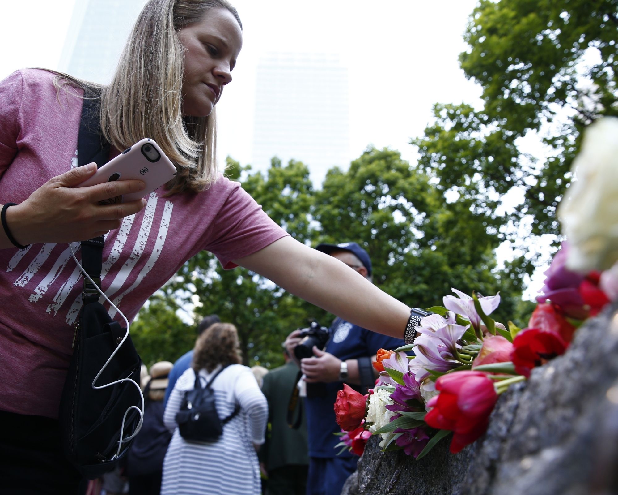 A woman in a pink tee shirt, with blonde hair, lays a flower on the Glade