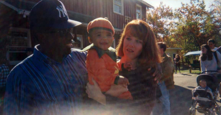 A mother and father hold their infant daughter who is dressed as a pumpkin for Halloween. 