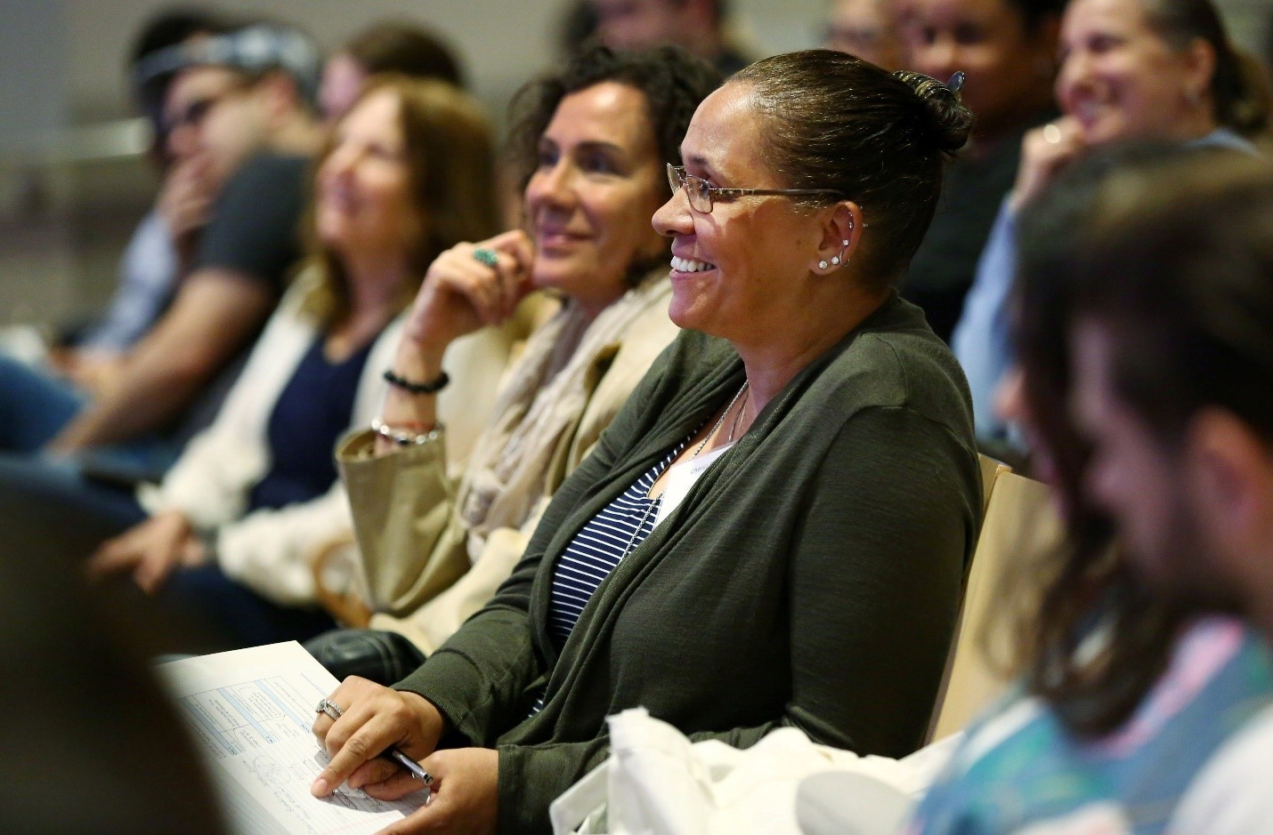 A row of attendees smiling as they watch an unseen presentation 