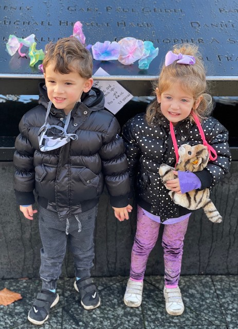 Two small children - a boy and a girl - stand in winter coats at the 9/11 Memorial.