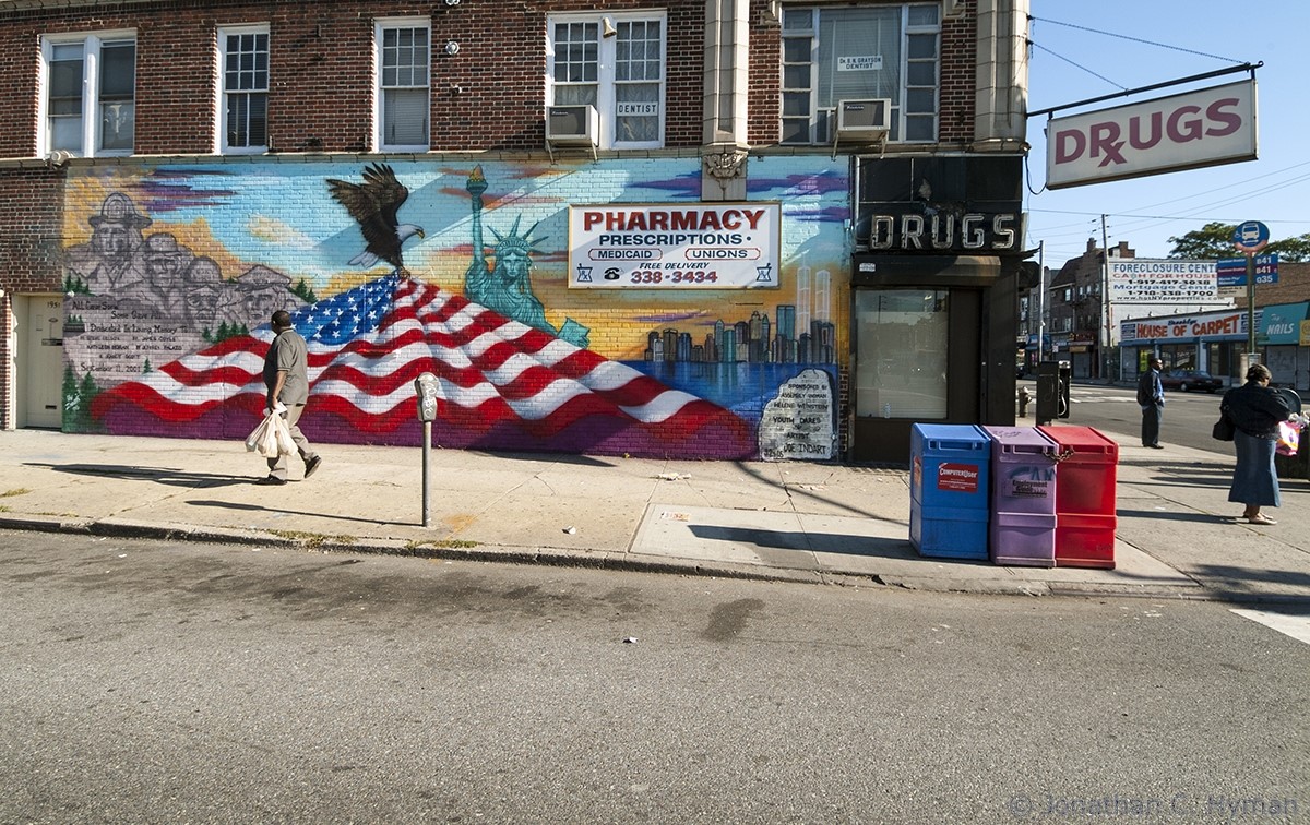 Mural featuring Mount Rushmore figures wearing first responder hats; a large unfurling American flag; the Statue of Liberty; and the New York skyline.