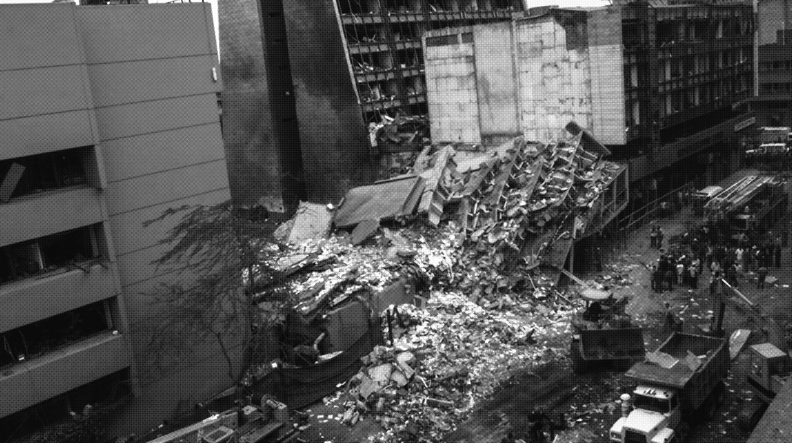 An aerial view of a destroyed building between partially damaged buildings.