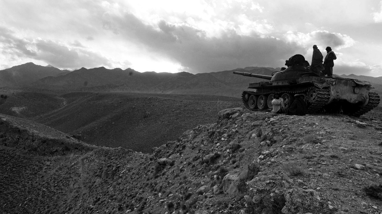 Two individuals standing on a tank overlooking a rocky desert landscape.