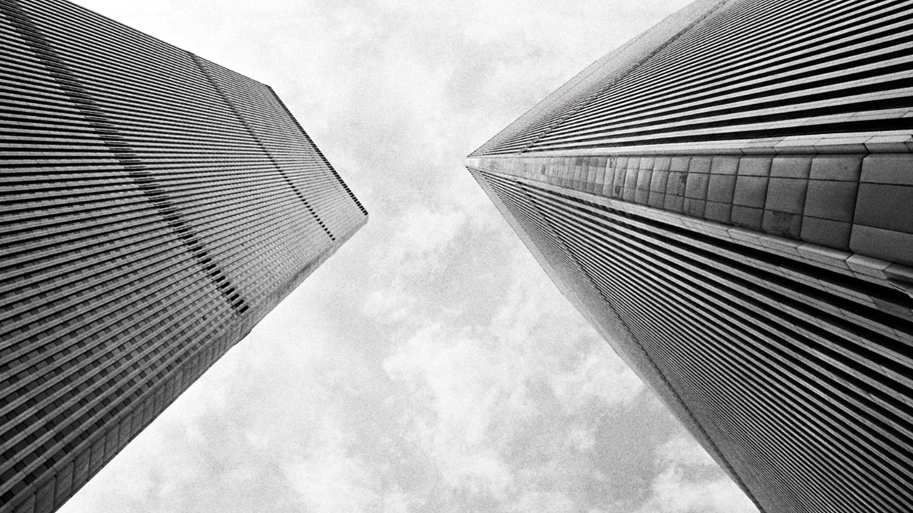 Low-angle view of the Twin Towers roaming into the cloudy sky. The height is emphasized by the towers' chamfered corners and closely spaced exterior columns.