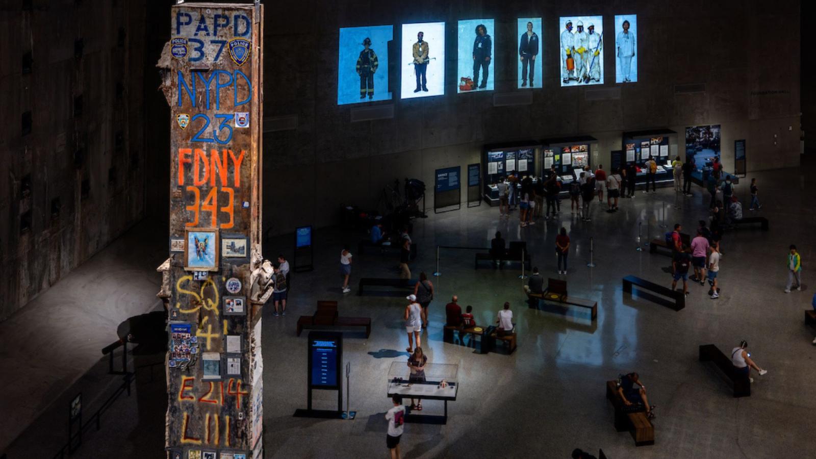 View of Foundation Hall showing the Last Column, visitors milling, display cases, and large-scale projected images in the background