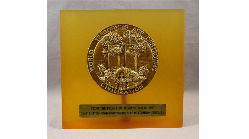 Orange-hued square plague with bronze seal in the upper center depicting the Twin Towers with smoke billowing out. Text written around the seal reads: "World terrorists are destroying civilization."